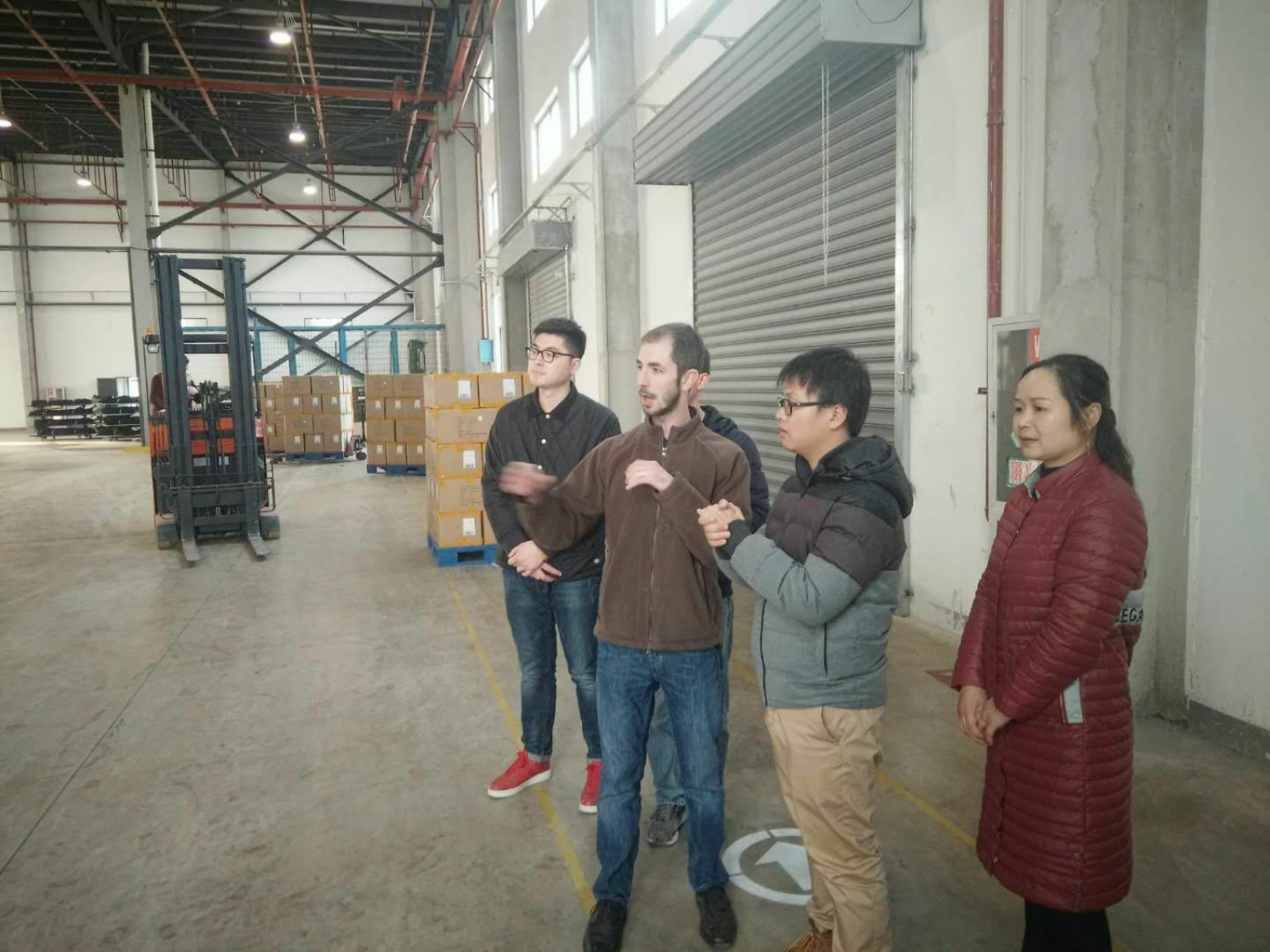 A group discussing work inside a warehouse beside stacked boxes and equipment